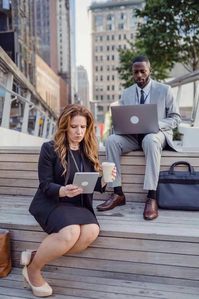 Two business professionals using technology outdoors in a city setting.