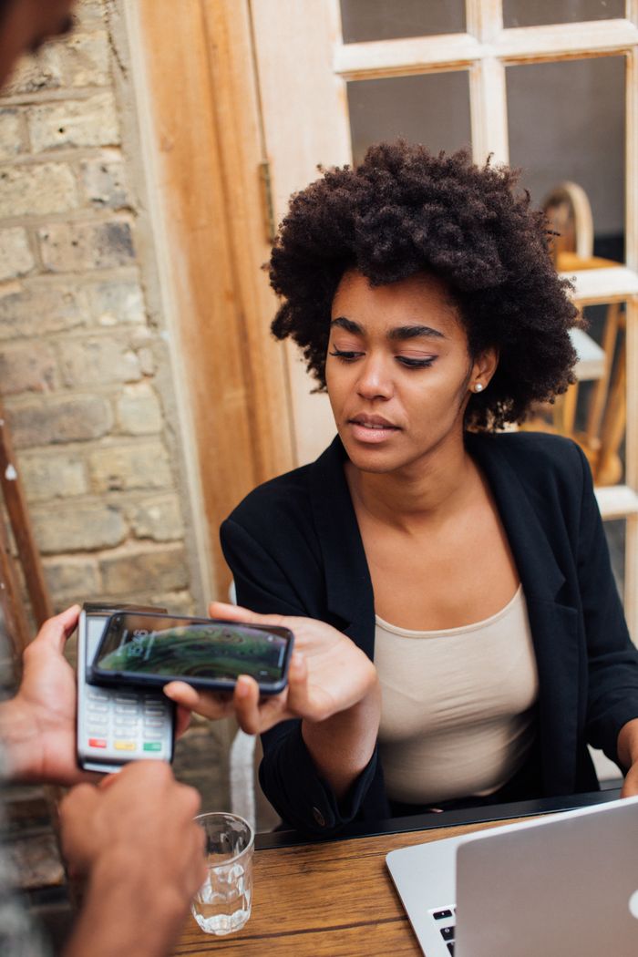An African American woman uses a phone for a cashless transaction at a cafe.