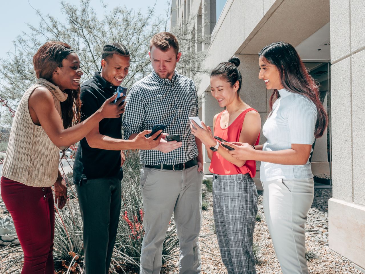 Crafting Captivating Headlines: Your awesome post title goes here A diverse group of colleagues smiling and engaging with smartphones outside an office building.